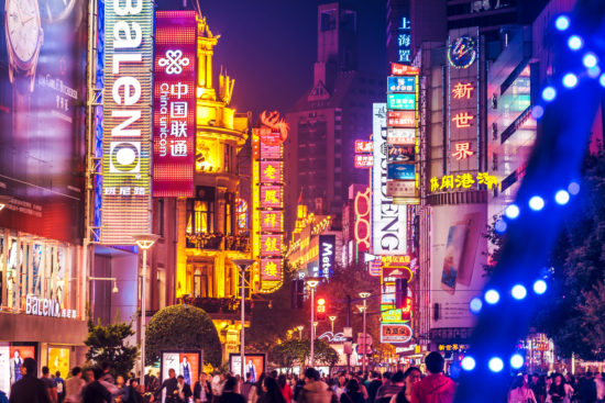 Crowds walk below neon signs on Nanjing Road. The street is the main shopping district of the city and one of the world's busiest shopping districts.